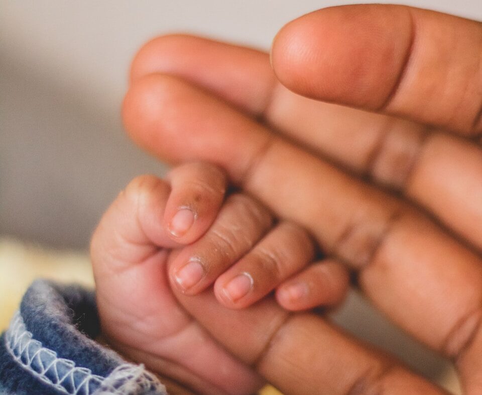 child's hand gripping person's pinkie finger